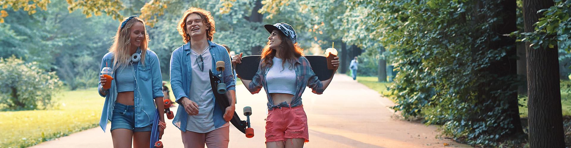 Cuenta Joven In - Grupo de jovenes vestidos con ropa moderna con patinetes, sonriendo junto a un parque rodeado de arboles