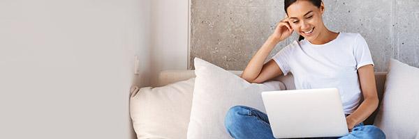 Préstamos Particulares - Mujer joven con su portatil en el sofa de su casa sonriendo Préstamos Particulares - Mujer joven con su portatil en el sofa de su casa sonriendo
